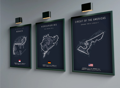 Three framed maps of different race tracks on a gray wall with lights.